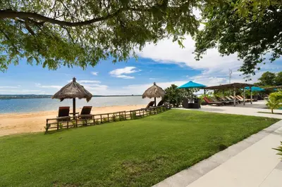 a beach with chairs and umbrellas on the grass at Peninsula Bay Resort in Nusa Dua