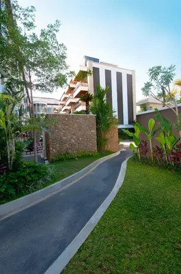 a road in front of a building with trees at Quest San Denpasar by ASTON in Denpasar