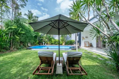 two chairs under an umbrella next to a pool at Villa Kangaroo Seminyak next to double six beach in Seminyak