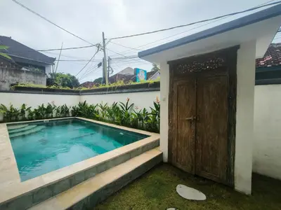a house with a swimming pool next to a door at Ken Ken Guest House in Seminyak
