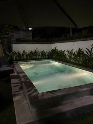 a swimming pool in a backyard at night at Ken Ken Guest House in Seminyak