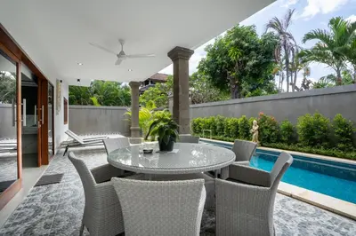 a patio with a table and chairs next to a swimming pool at Aster Villa by iBali Management in Legian