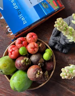 a bowl of fruit on a table next to a book at Oemah Djoglo Kerobokan in Kerobokan