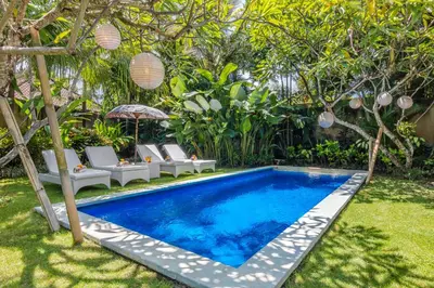 a swimming pool in a yard with chairs and trees at Villa Lodek Deluxe in Seminyak
