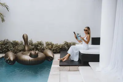a woman sitting on a bed reading a book next to a pool at Villa Manis Kecil in Seminyak