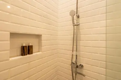 a shower in a bathroom with white brick walls at Adikara Apartment by Betterplace in Canggu