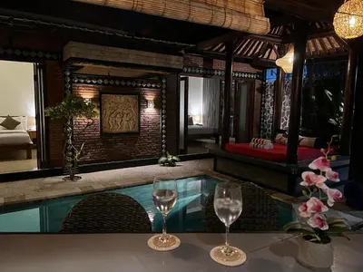 two wine glasses sitting on a table next to a pool at Villa Mutti in Seminyak
