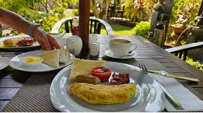 a table with a plate of breakfast food on it at Frangipani Homestay in Nusa Dua