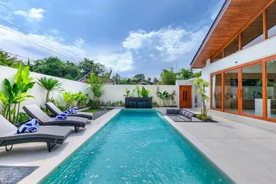 a swimming pool with lounge chairs and a house at The Aurum Canggu Villas by Nagisa Bali in Canggu
