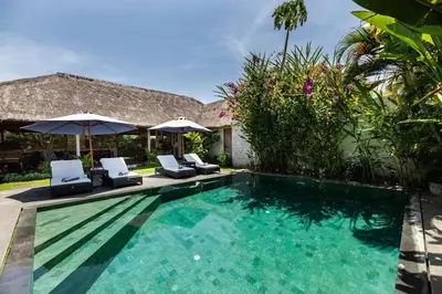 a pool with chairs and umbrellas next to a house at Villa Damai Manis in Seminyak