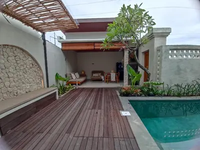 a house with a wooden deck and a swimming pool at Villa Juanjo Sanur in Sanur