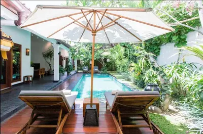 a pool with chairs and an umbrella next to a swimming pool at The Clovewood Villa in Seminyak