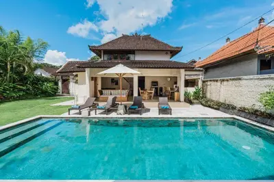 a pool in front of a house with chairs and an umbrella at 10 Bedroom Villa Vista Seminyak in Seminyak