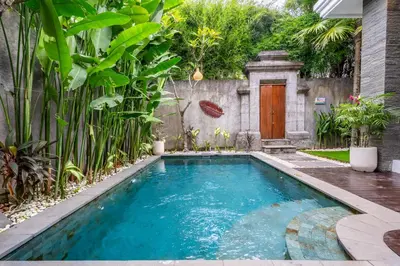 a swimming pool in a garden with a wooden door at Villa Bima by JB Villas in Seminyak