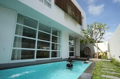 two people in a swimming pool in front of a house at The Cendana Villa Umalas in Badung