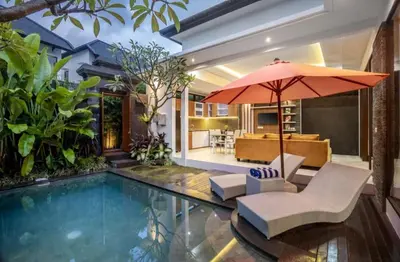 a pool with a chair and an umbrella next to a house at Puri Sahadewa Seminyak in Seminyak