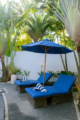 two blue lounge chairs with an umbrella and palm trees at Peaceful 2br with pool & garden in Seminyak