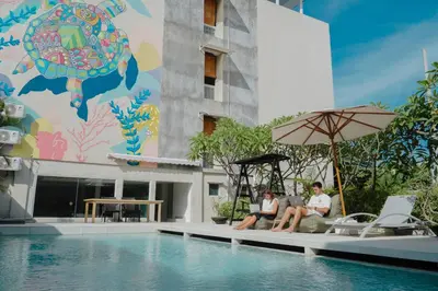 two people sitting under an umbrella next to a swimming pool at Bali Bustle Kuta Coliving & Coworking Space in Legian