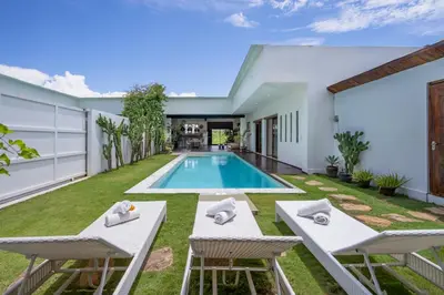 a backyard with a swimming pool and two chairs and a house at Villa Nuga By DreamAwayBali in Seminyak