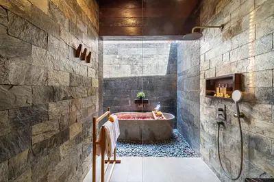 a bathroom with a tub and a stone wall at Villa Bolon in Kuta
