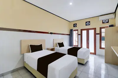 two beds in a room with two windows at Townhouse Oak Legian Near Kuta Beach Formerly Sayang Maha Merta in Legian