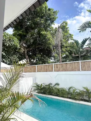 a swimming pool with a fence and trees at The Pink Door Villa in Legian