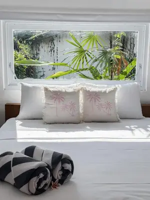 a white bed with four pillows and a window at The Pink Door Villa in Legian