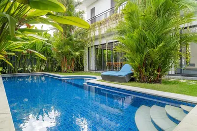 a swimming pool in front of a building with palm trees at Villa Damai Canggu in Seminyak