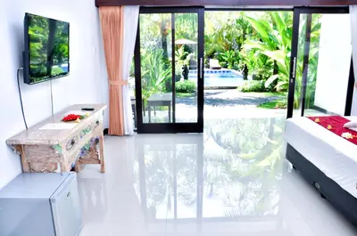 a room with a bed and a table and a window at Palm Garden Bali in Nusa Dua