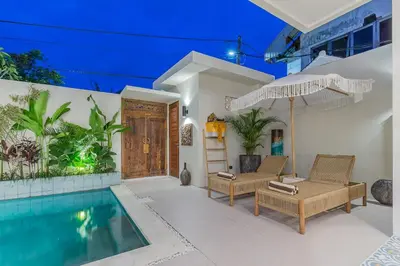 a house with a swimming pool and two chairs and an umbrella at Villa Pop Cozy 2BR Villa & Pool Seminyak in Seminyak