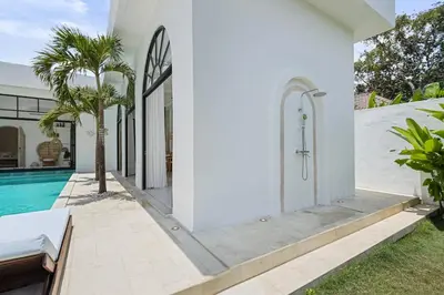 a white house with a swimming pool and palm trees at Chic All-White Villa with Pool and Fire Pit in Jimbaran