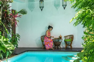 a woman sitting at a table next to a pool at The Cottage By Selasih in Seminyak