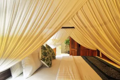 a canopy bed with white curtains in a bedroom at The Cottage By Selasih in Seminyak