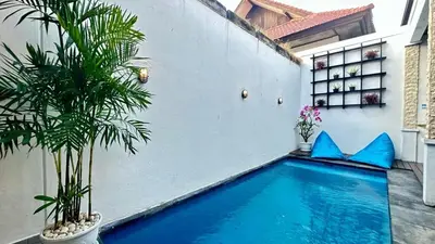 a swimming pool in front of a white wall with a plant at 2 Bedrooms Villa Petitenget Private Pool in Seminyak