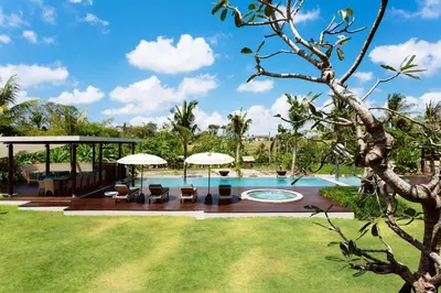 a pool with chairs and umbrellas in a yard at Umah Daun by Nakula in Canggu