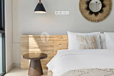 a bedroom with a bed with a wooden headboard and a table at Sariha by Kozystay - Nusa Dua in Nusa Dua