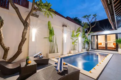 an outdoor swimming pool with chairs and a table at Villa Kunti in Seminyak