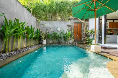 a swimming pool with an umbrella in a backyard at Villa Yudhistira by JB Villas in Seminyak