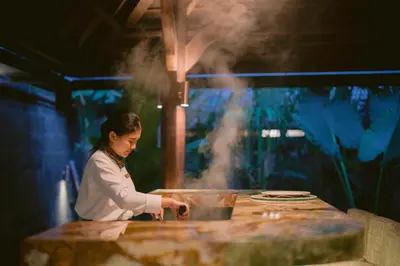 a woman cooking food on a table with smoke at The Suaka Baliaga by Puri Asia in Seminyak