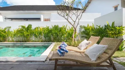 a wicker chair sitting next to a swimming pool at Villa Lange 3 by Villa Finder in Seminyak