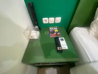 a green table next to a bed with a remote control at AI Hotel Kuta - 15 Second to the Beach and 1 Minute to Airport by Micky Studio in Ngurah Rai International Airport