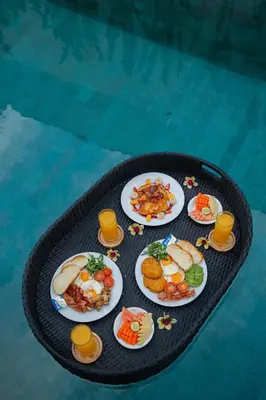 a table with plates of food on a table next to a pool at Arvi Villa Pandawa Legian in Legian