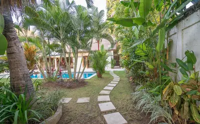 a garden with a swimming pool and palm trees at Villa Umah Maya in Seminyak