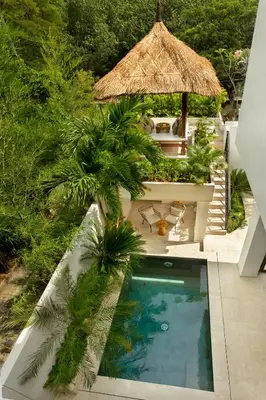 an outdoor swimming pool with a straw umbrella and palm trees at Balidroomvilla Sanur Mangrove - Full Serviced - Beachside in Sanur
