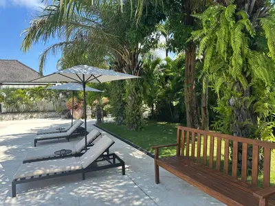 a group of benches with an umbrella and trees at Nature's Immersion Room at Anwa Bali Boutique Resort in Canggu
