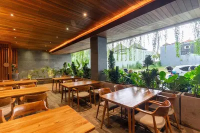 a restaurant with wooden tables and chairs and a large window at LOI Mansion Managed by ARM One Hundred in Seminyak
