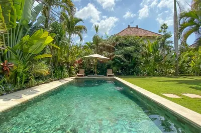 a swimming pool with two chairs and an umbrella in a yard at Two bedroom Villa in a beautyful tropical garden in Seminyak