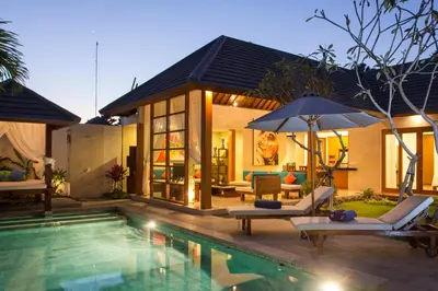 a house with a swimming pool with two chairs and an umbrella at Bunga Neil Villa in Seminyak