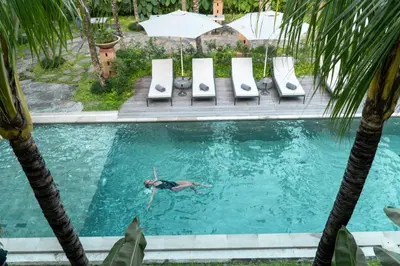 a man swimming in a swimming pool next to palm trees at Anam Tang New Rooms & Cafe near Seminyak in Seminyak