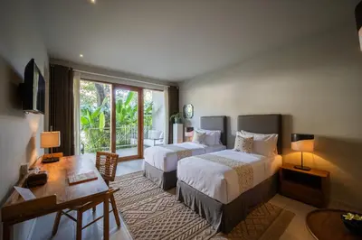 a hotel room with two beds and a desk and a window at Anam Tang New Rooms & Cafe near Seminyak in Seminyak